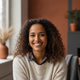 A smiling woman in smart casual attire, headshot portrait, against a blurred background with warm earthy tones.